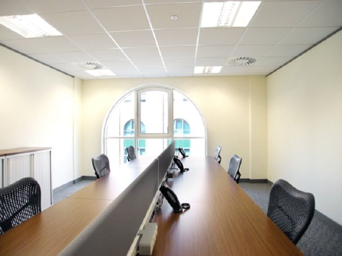 A bright, modern office space with long wooden desks and mesh chairs in Pepper Street 16, London.