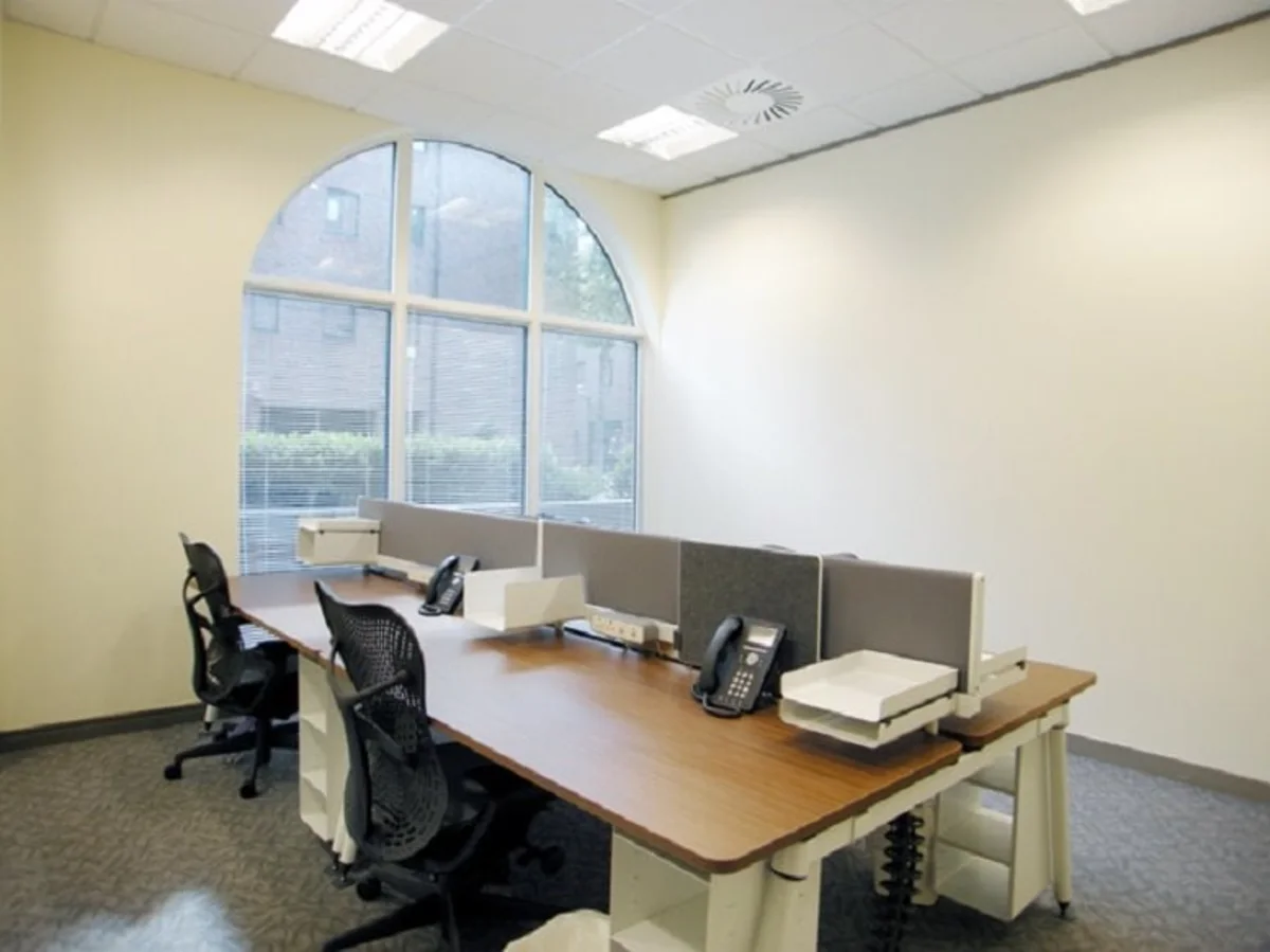 Modern office space with desks and chairs near a large arched window.