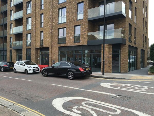 Modern apartment building with glass balconies and parked cars along Plough Way in London.