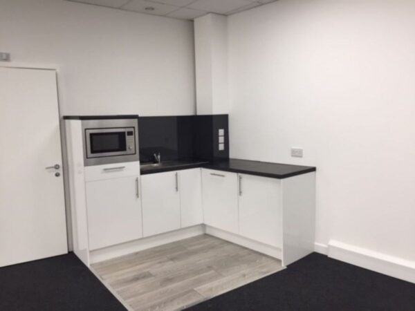 A small kitchenette with white cabinets and a microwave in a modern office space at Plough Way Units A B, London.