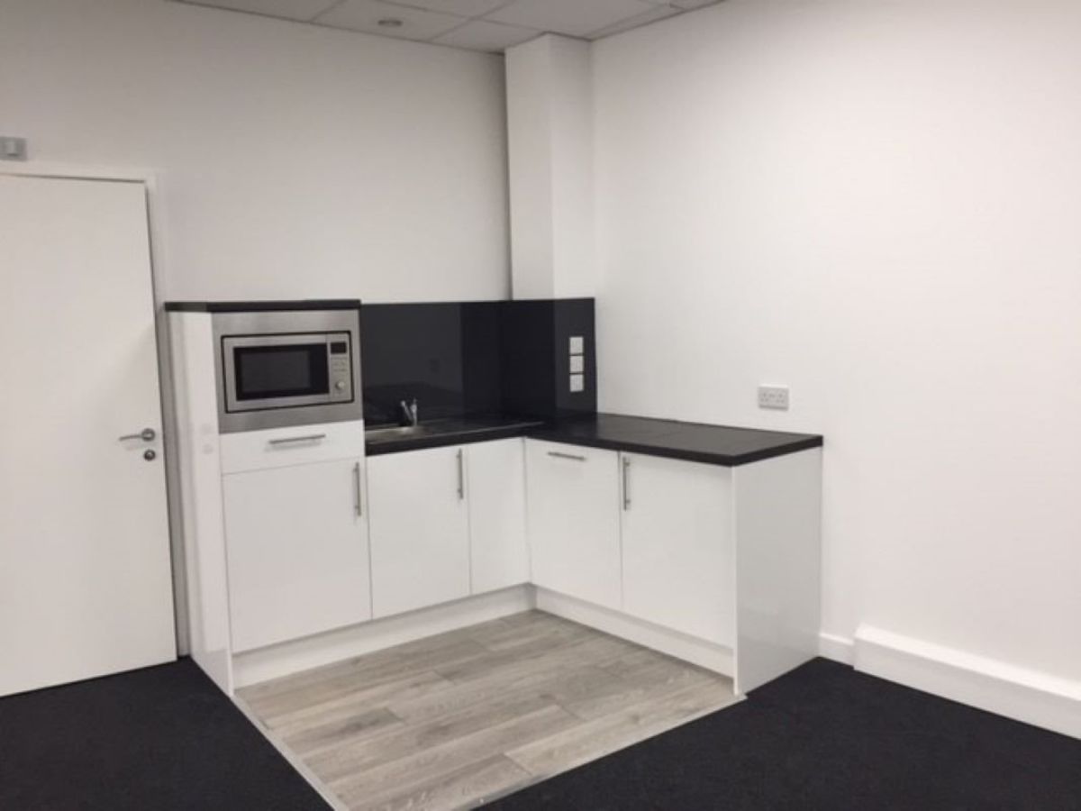A small kitchenette with white cabinets and a microwave in a modern office space at Plough Way Units A B, London.