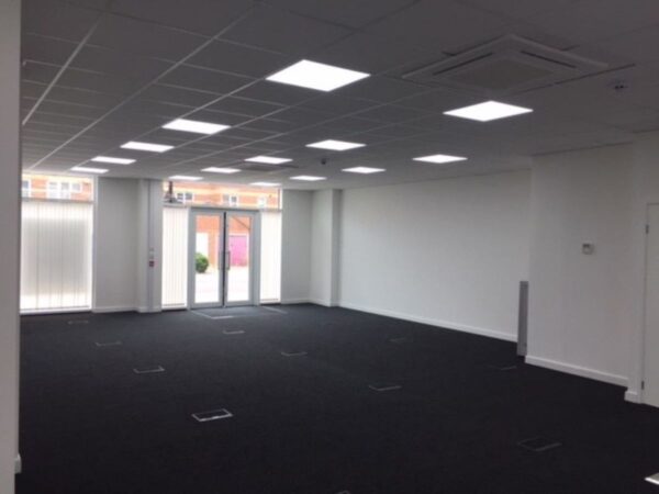An empty office space with white walls, a black carpet, and large windows at Plough Way Units A and B in London.