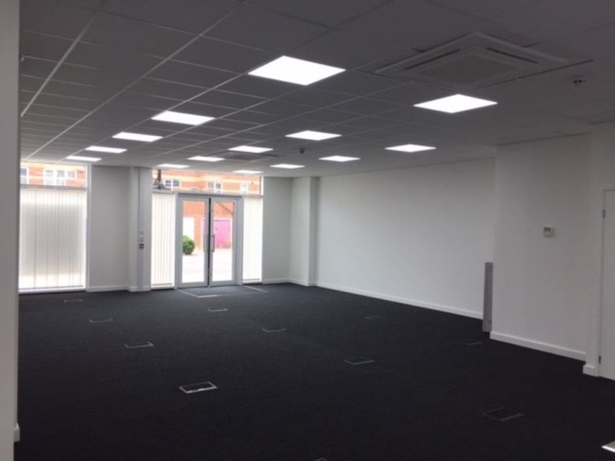 An empty office space with white walls, a black carpet, and large windows at Plough Way Units A and B in London.