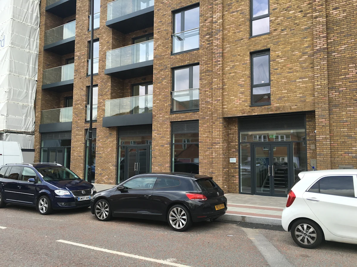 The exterior of Plough Way Units A and B in London, featuring modern brick architecture with glass balconies and parked cars in front.
