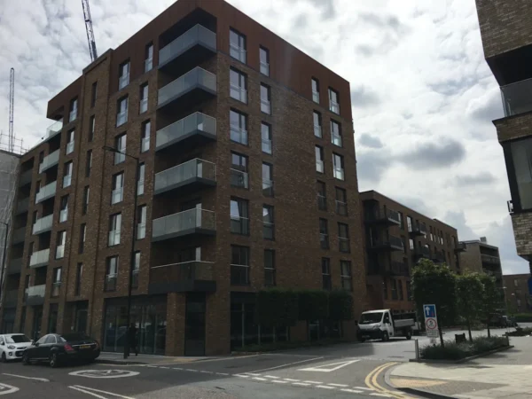 Modern apartment buildings on Plough Way, London, with parked cars and nearby street signage.
