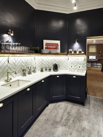 A stylish, modern kitchen with dark cabinets and a herringbone-tiled backsplash, featuring a framed picture of a red London bus.