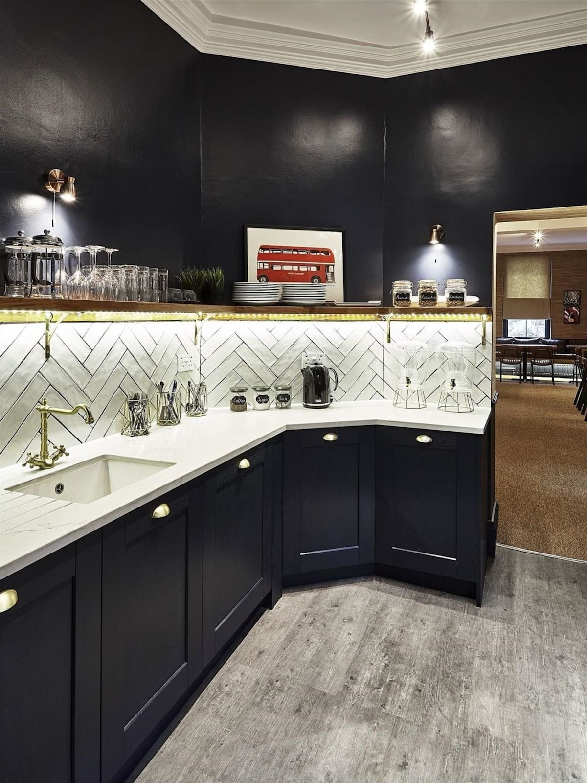 A stylish, modern kitchen with dark cabinets and a herringbone-tiled backsplash, featuring a framed picture of a red London bus.