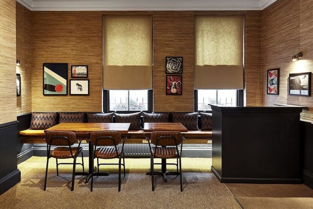 A cozy dining area with wooden tables, leather chairs, art-adorned walls, and large windows.