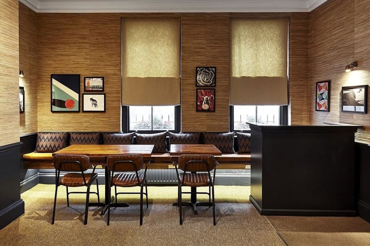 A cozy dining area with wooden tables, leather chairs, art-adorned walls, and large windows.