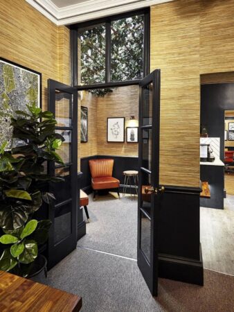 A stylish interior space with a glass double door, wooden walls, a plant, and artwork on the walls.