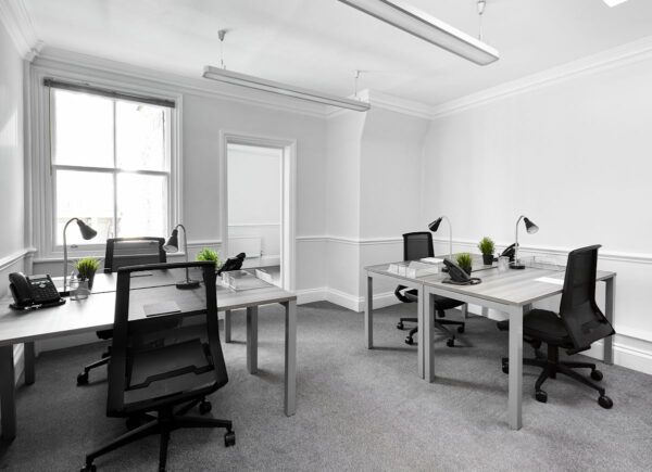 A modern, minimalist office space with desks, chairs, phones, desk lamps, and potted plants at Poland Street 54, London.
