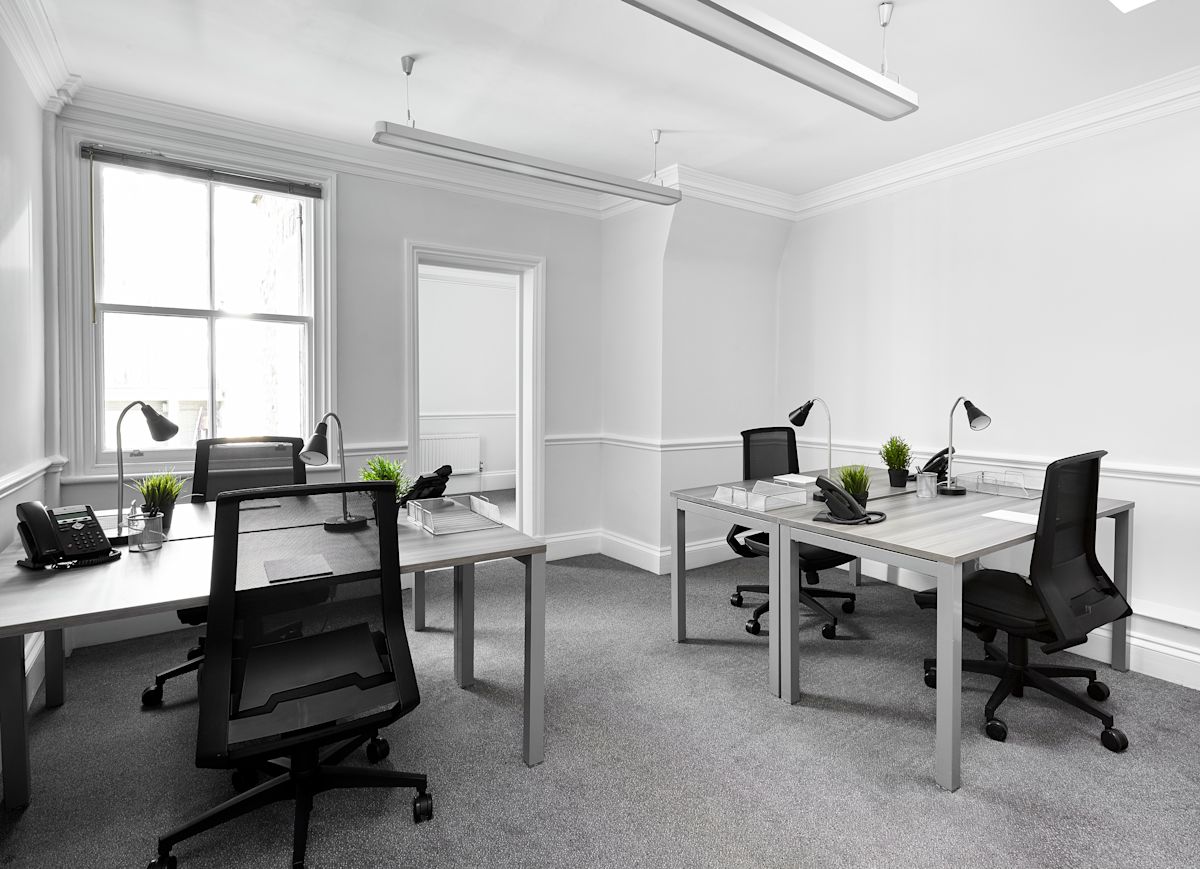 A modern, minimalist office space with desks, chairs, phones, desk lamps, and potted plants at Poland Street 54, London.