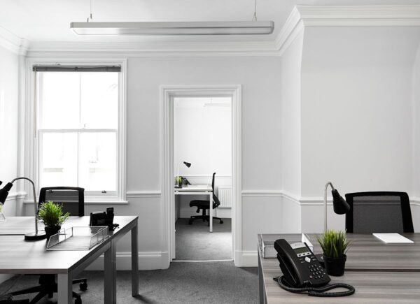 A bright, modern office space with desks, chairs, plants, and telephones on Poland Street 54 in London.