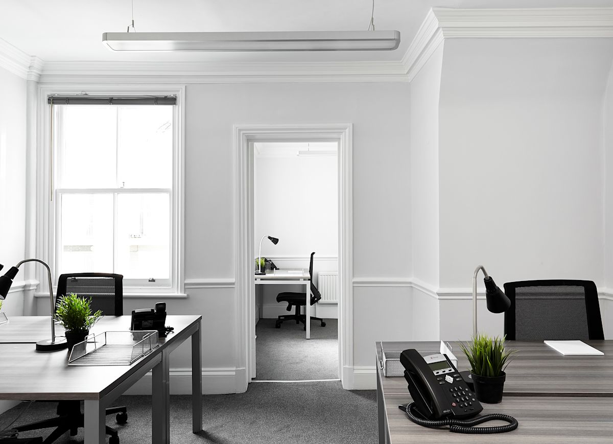 A bright, modern office space with desks, chairs, plants, and telephones on Poland Street 54 in London.