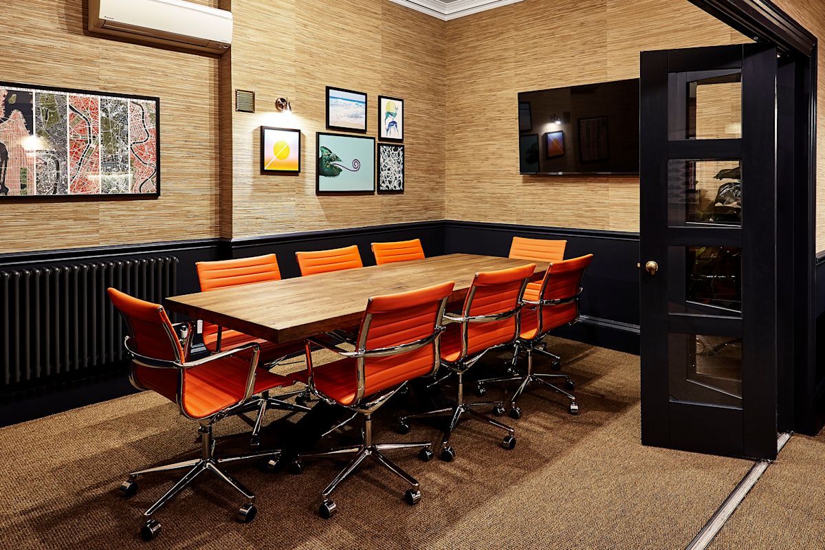 A modern meeting room with orange chairs and a wooden table at Poland Street 54, London.