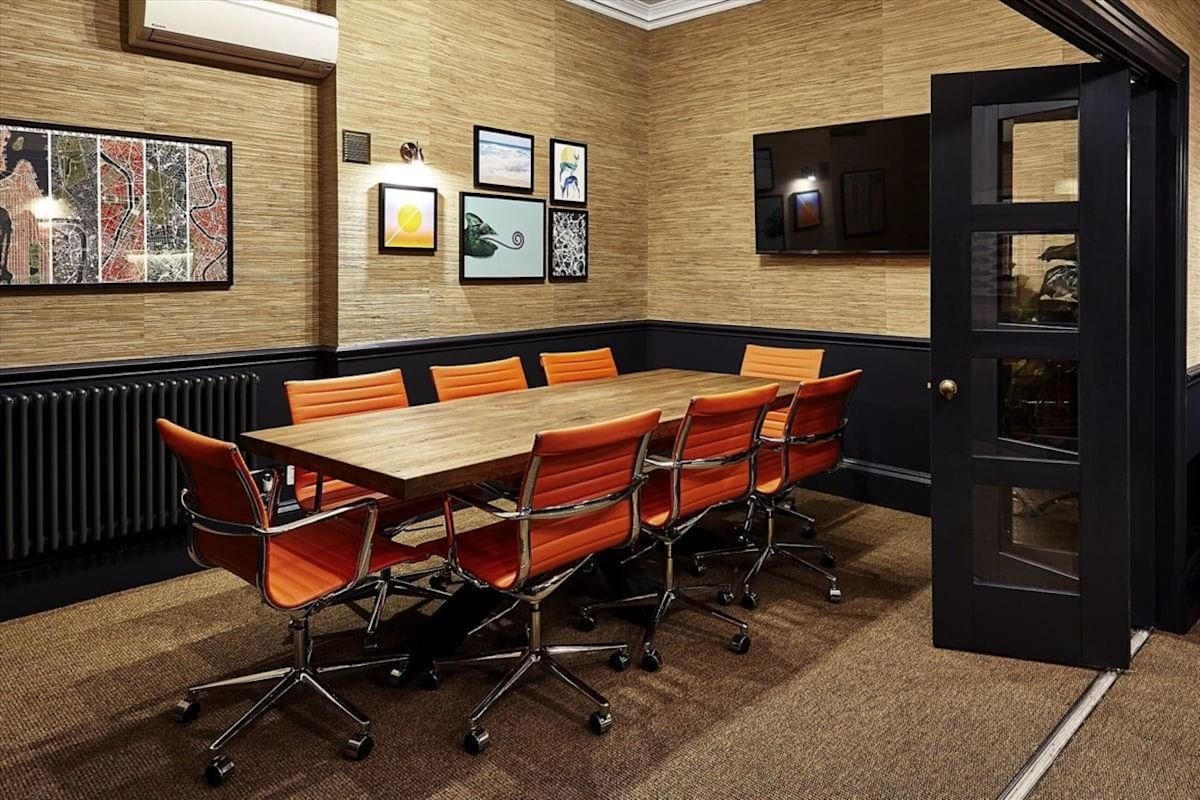 A modern conference room with a wooden table, orange chairs, and artwork on the walls.