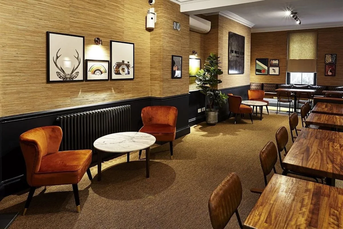 A cozy café interior on Poland Street 54, London, featuring wooden tables, orange chairs, and eclectic wall art.