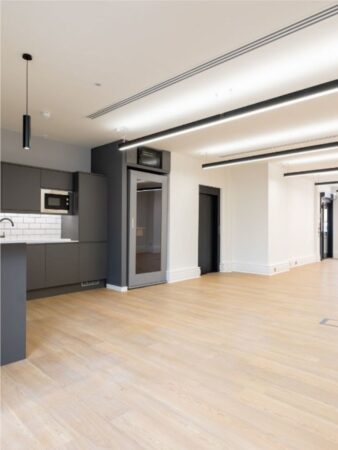 A modern, empty office space featuring light wooden flooring and a sleek kitchen area at Poland Street 6, London.