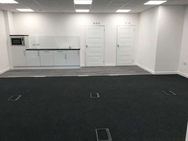 A modern, empty office space with a small kitchenette and two doors.