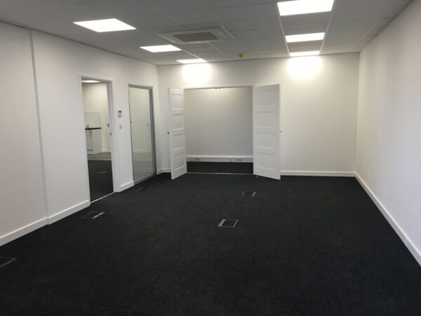 An empty, modern office space with white walls and dark carpet.
