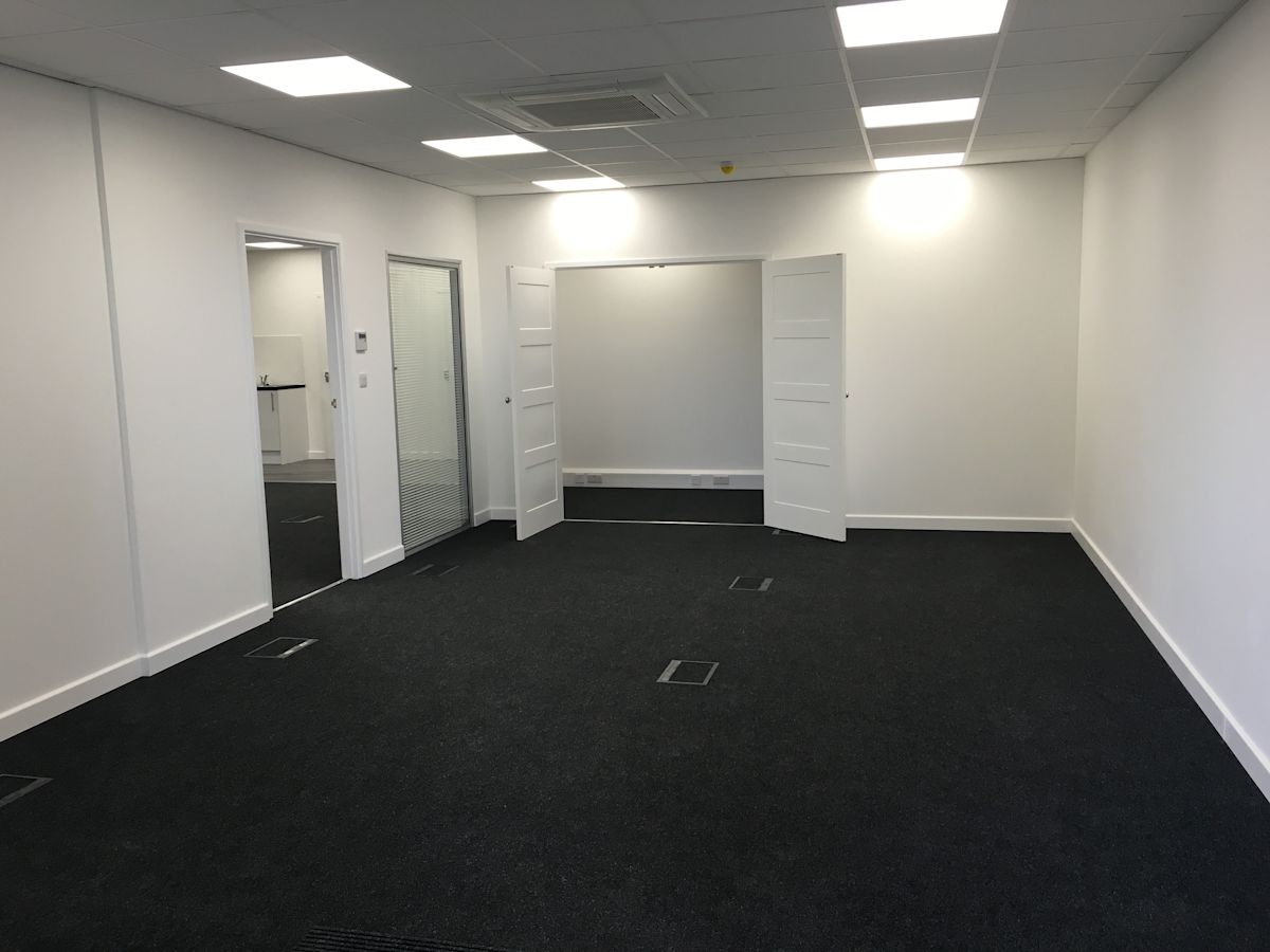 An empty, modern office space with white walls and dark carpet.