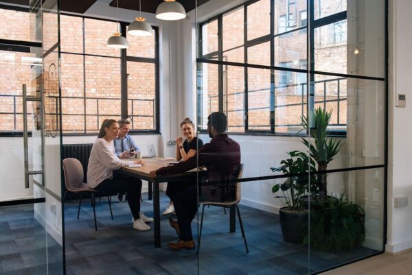 A group of people having a meeting in a modern office space with large windows and plants.