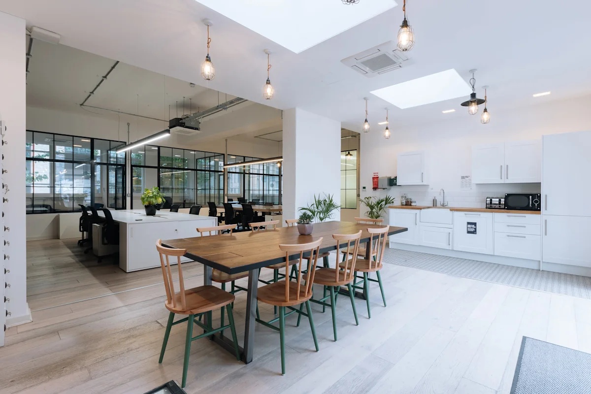Modern office interior featuring a communal table, kitchen area, and open workspaces.