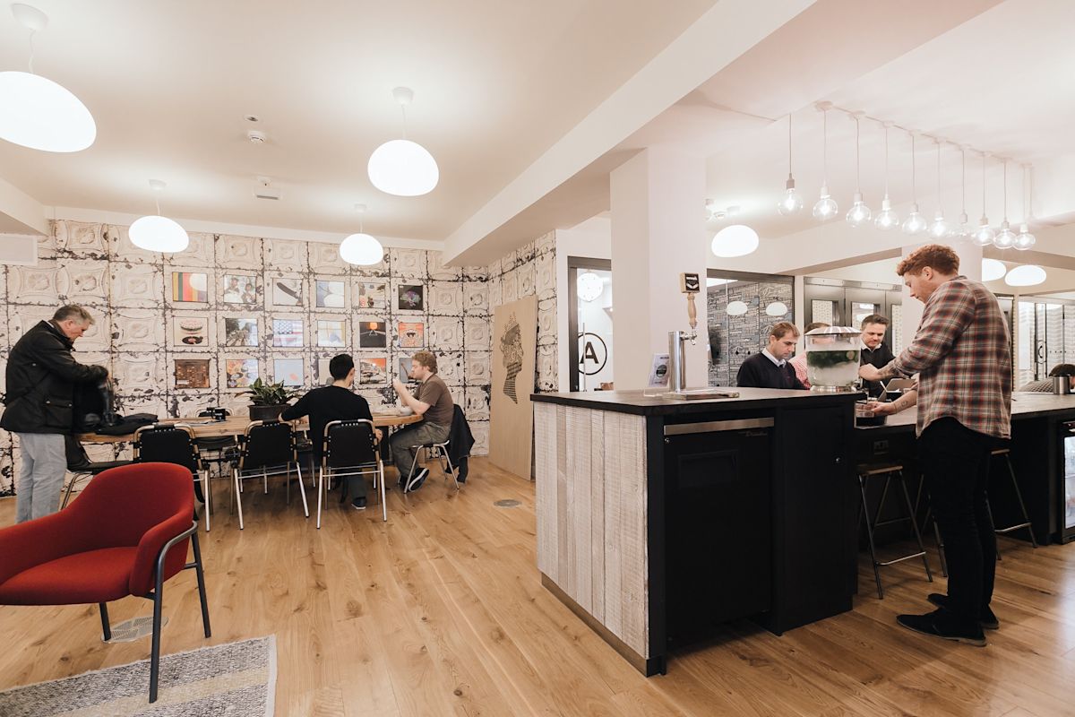 A modern, communal workspace in Sheraton Street, London, with people working and interacting.