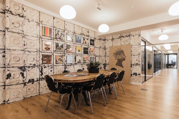 A modern meeting room with a wooden table, surrounded by chairs, and decorated with art on textured walls.