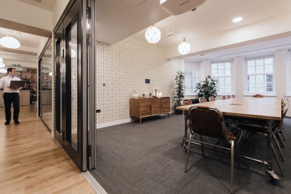 A modern office space with a large meeting table, decorative cabinet, and a person walking in the background.