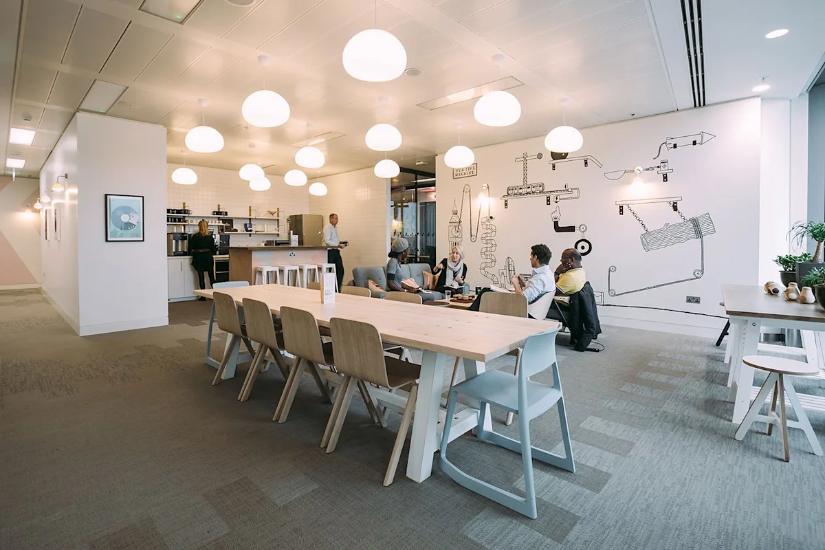 A modern office break room in London with a communal table, lounge area, and wall art.