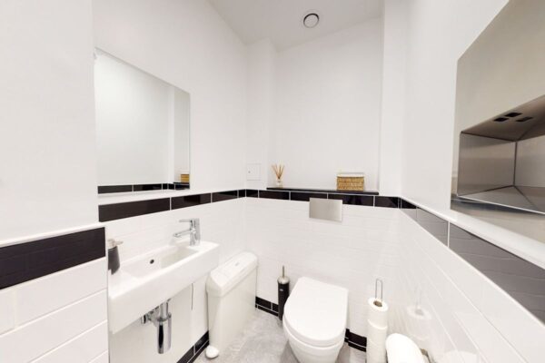 A modern bathroom with white tiles, a wall-mounted sink, and a toilet.
