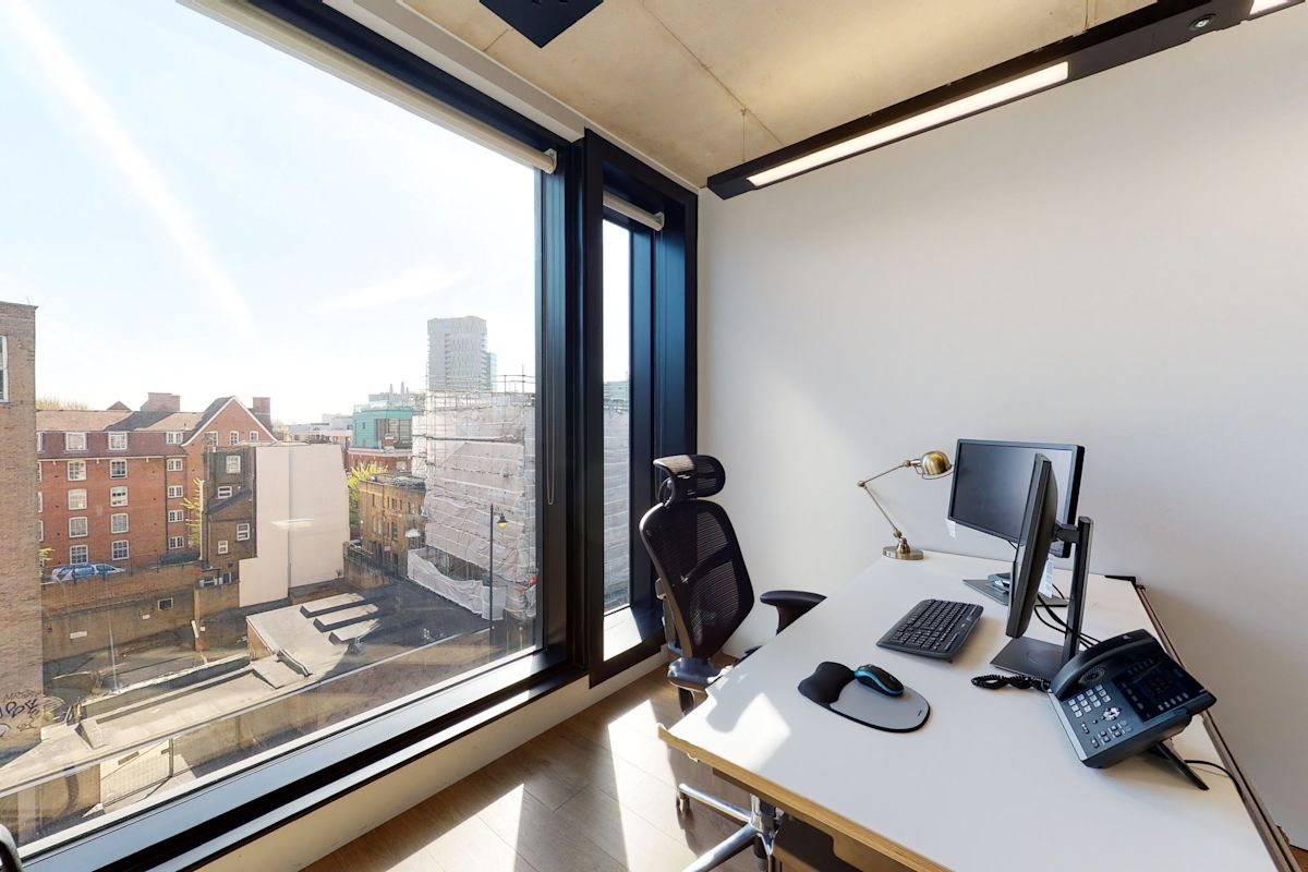 A modern office with a view of Shoreditch High Street, featuring a desk, chair, computer, and phone.