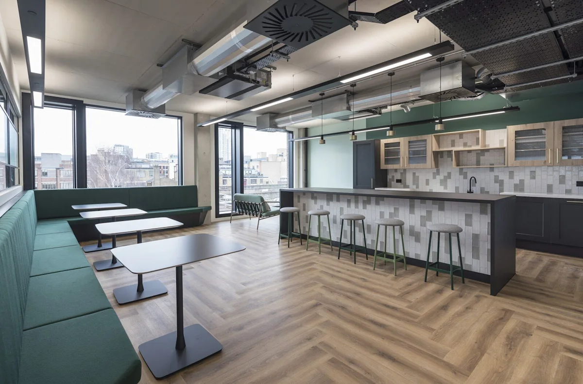 Modern office kitchen and dining area with green seating and wooden flooring at Shoreditch High Street 168, London.