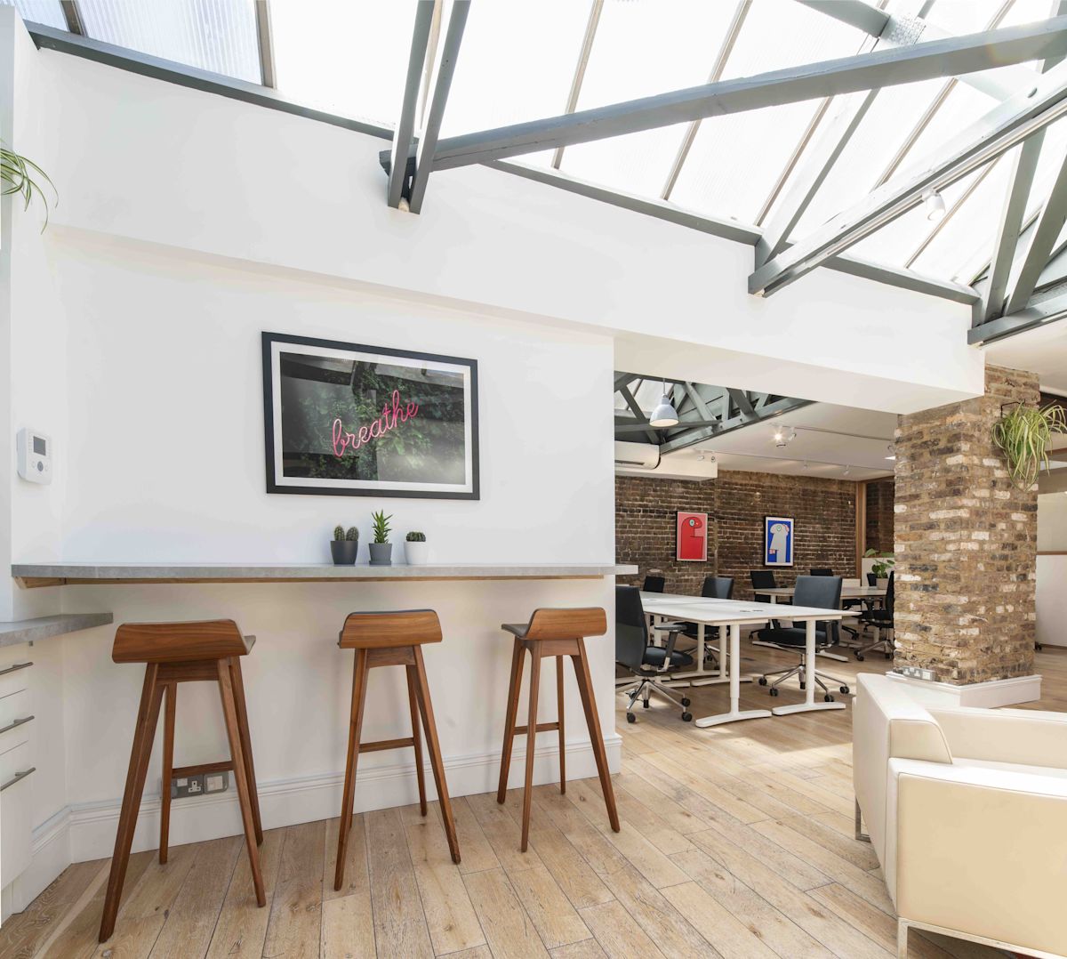 Modern office interior with high stools, desk area, and exposed brick walls under a skylight in Shoreditch High Street, London.
