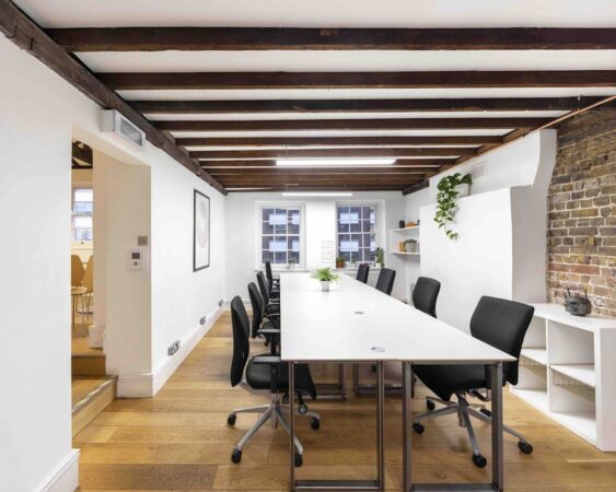 A modern office space with wooden floors, exposed beams, and a long table with black chairs.