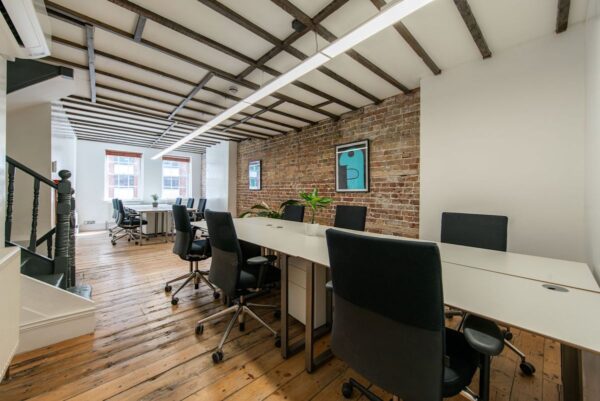 A modern office space with wooden floors, brick walls, and several desks with chairs in Shoreditch High Street, London.