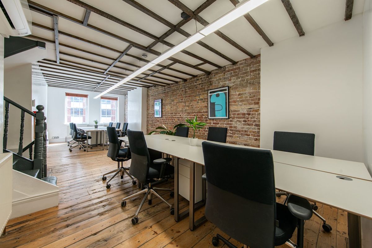 A modern office space with wooden floors, brick walls, and several desks with chairs in Shoreditch High Street, London.