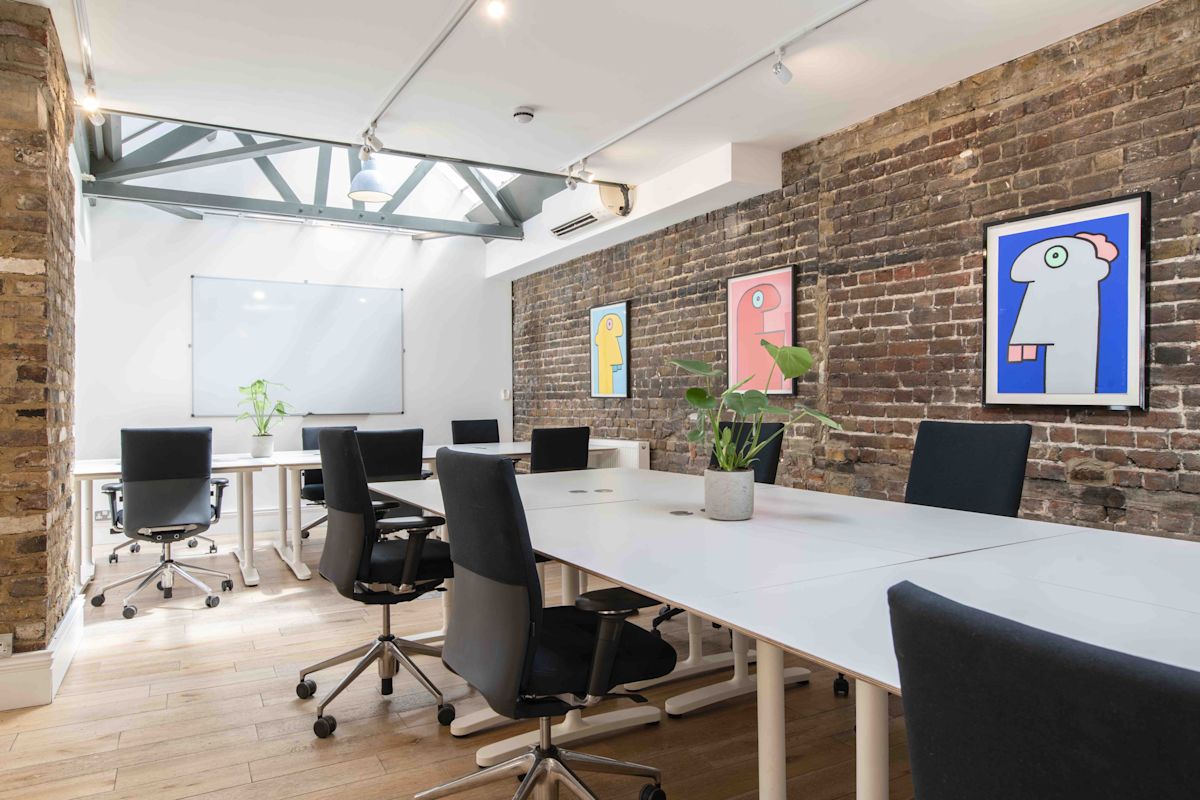A modern office space with brick walls, colorful abstract art, and sleek office chairs around a large table.