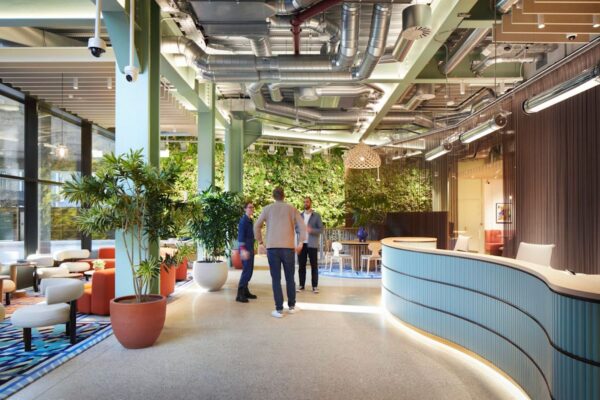 A modern and stylish lobby interior on Shoreditch High Street, London, featuring green plants and a small group of people talking.