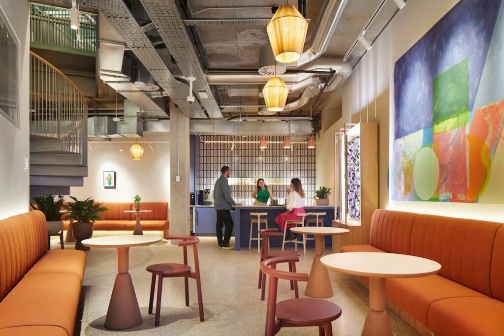 A modern lounge area in Shoreditch High Street, London, featuring colorful seating, abstract wall art, and three people at a bar counter.