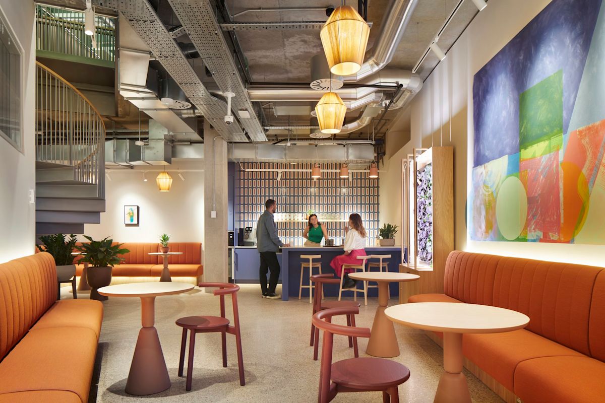 A modern lounge area in Shoreditch High Street, London, featuring colorful seating, abstract wall art, and three people at a bar counter.