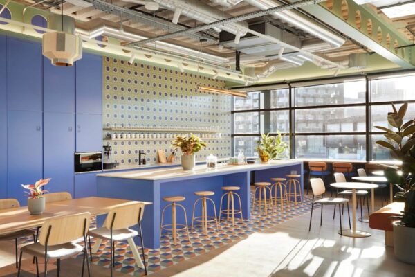 Modern office kitchen in Shoreditch High Street, London, featuring blue cabinets, patterned tiles, and wooden stools.