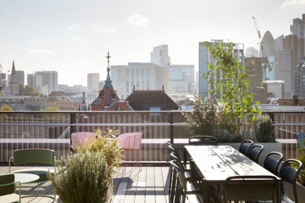 Rooftop terrace with plants and seating, overlooking the skyline of Shoreditch High Street, London.