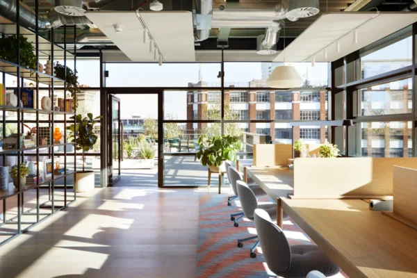 A modern, sunlit office space in Shoreditch High Street, London, featuring large windows and greenery.