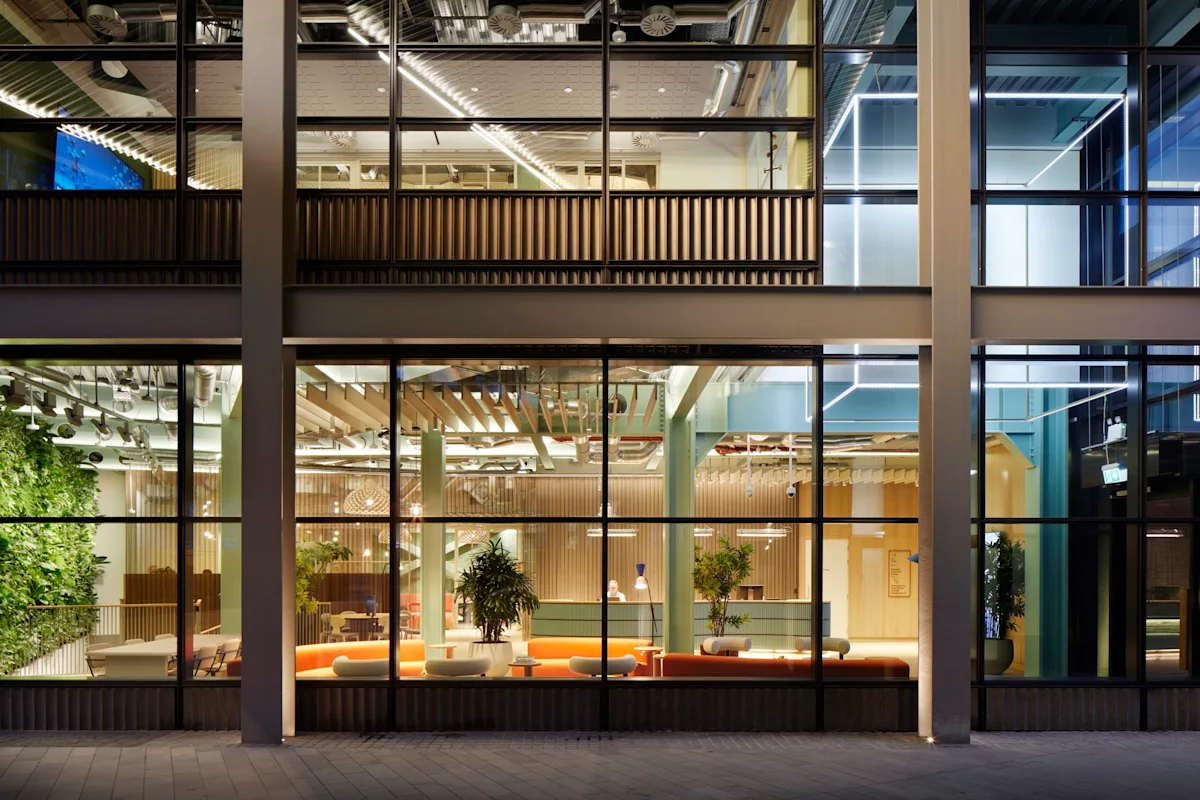 View of a modern office building with large glass windows and interior lighting on Shoreditch High Street, London.
