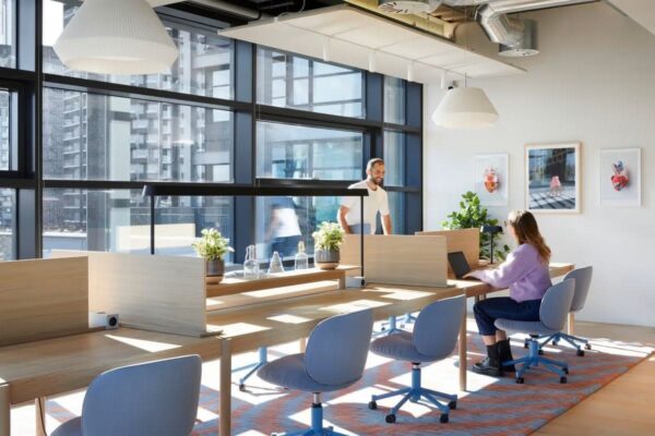 A modern, sunlit office space in Shoreditch High Street Montacute Yards, London, with people working at desks.