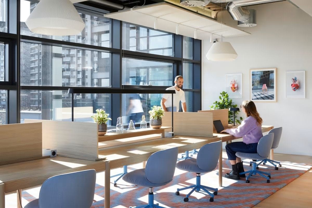 A modern, sunlit office space in Shoreditch High Street Montacute Yards, London, with people working at desks.