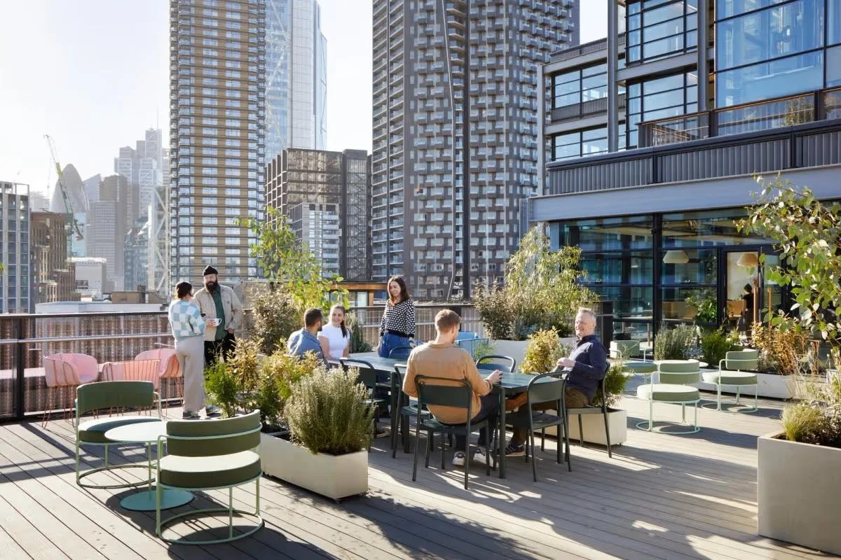 People relaxing and conversing on a rooftop terrace with a view of tall buildings in Shoreditch, London.