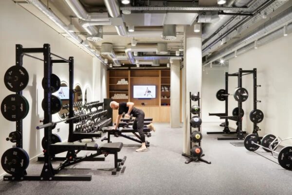 A modern gym with weightlifting equipment and a person exercising at Montacute Yards, Shoreditch High Street, London.